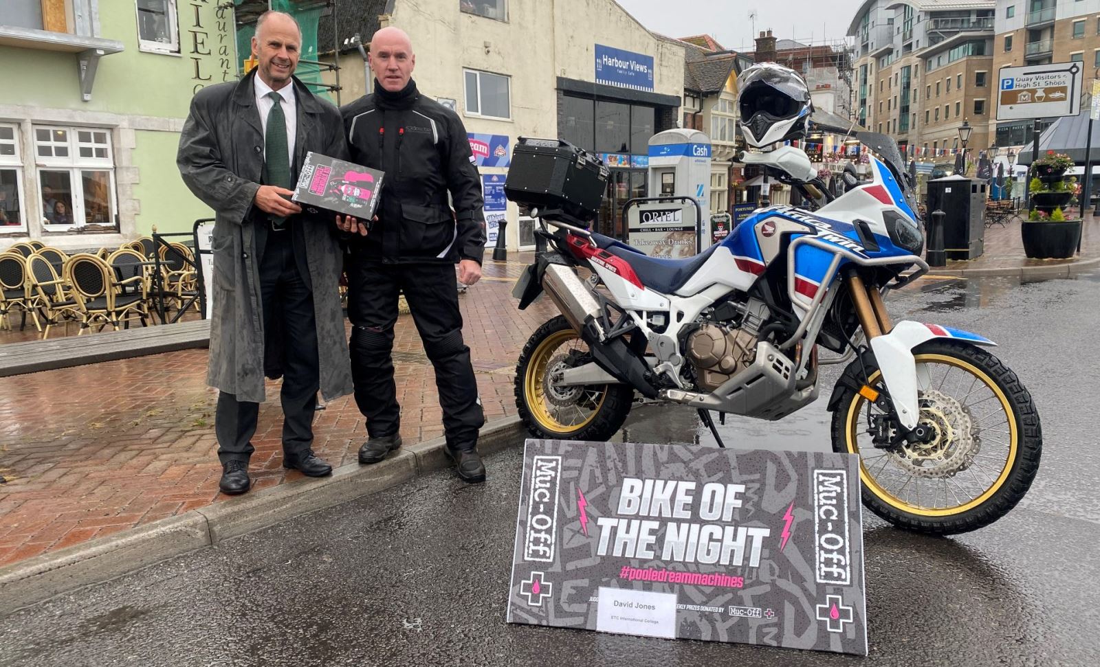 Two men posing with winning bike on a rainy day at Poole quay 